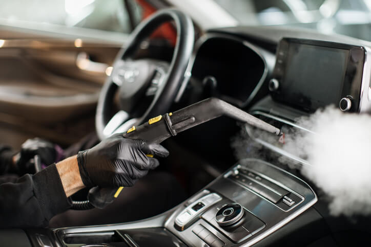 Detailer steam cleaning a car’s dashboard after auto detailing training