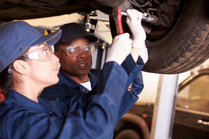A female pre-apprenticeship candidate conducting tire repair under the guidance of a seasoned auto mechanic.