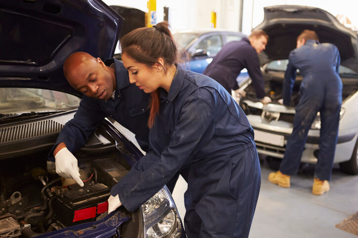 A female pre-apprenticeship candidate conducting tire repair under the guidance of a seasoned auto mechanic.