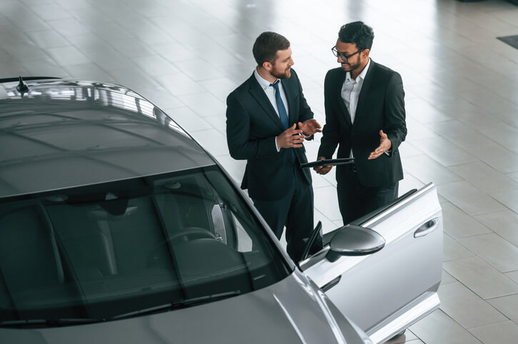 A smiling male auto salesman communicating with a customer after automotive sales training.