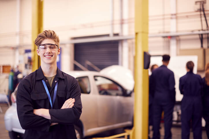 A smiling male student in automotive technology training helping as a shop helper.