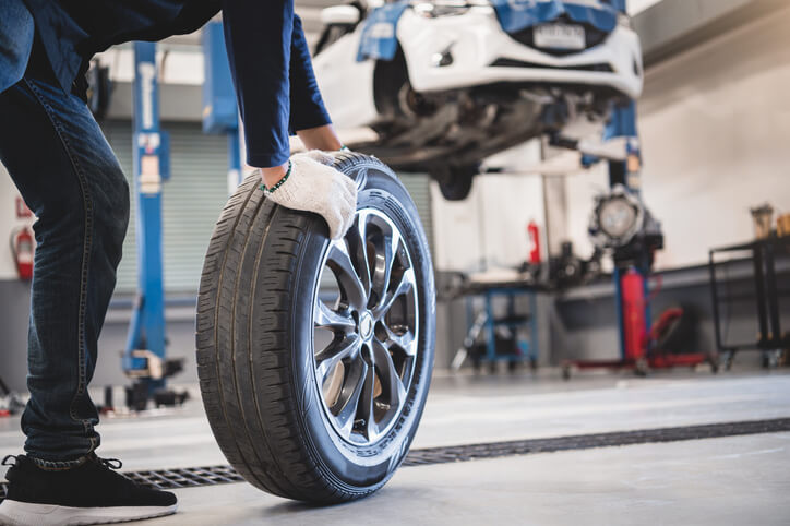 A student in automotive technology training fetching a tire while changing a wheel.