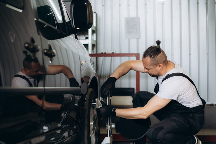 An auto mechanic trainee working on a vehicle’s alignment in automotive technology training.