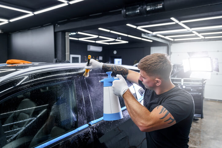 A student in automotive school training as an auto detailer working on the exterior of a vehicle before applying a treatment.