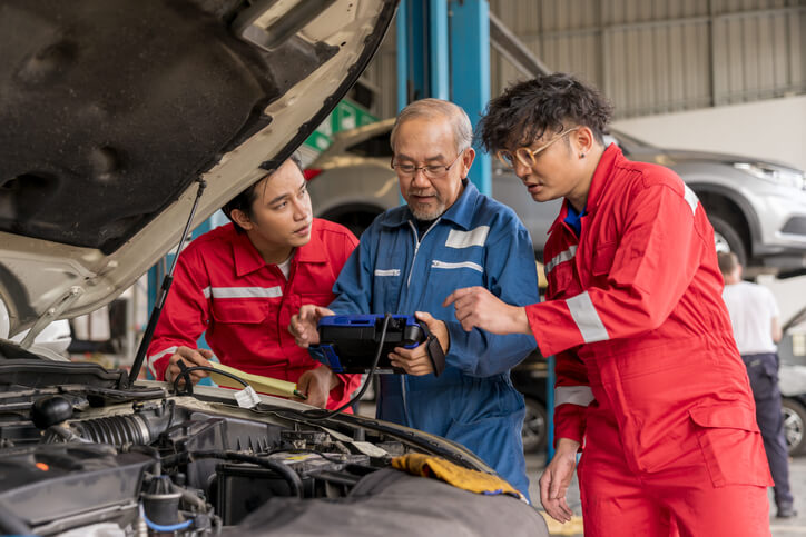 A team of auto mechanics preparing to work on a vehicle in an auto mechanic school