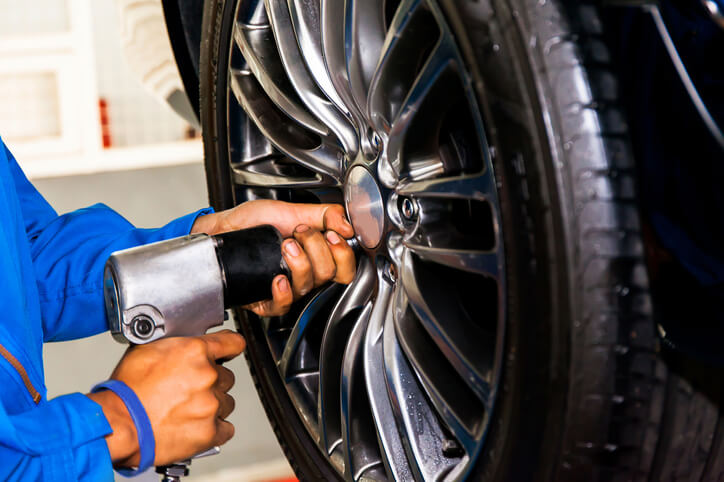After auto mechanic training, A male auto mechanic tightens lug nuts on a vehicle.