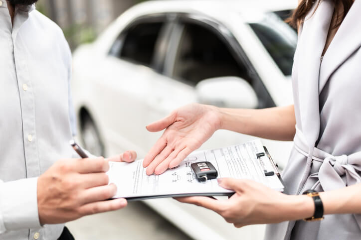 An auto salesperson handing car keys and a leasing agreement to a customer after automotive sales and leasing training.