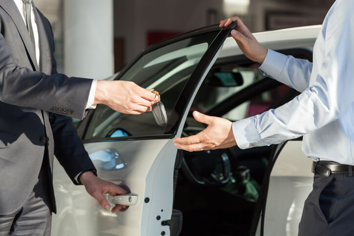 An auto salesman handing over a set of car keys to a buyer at a dealership after automotive sales training.