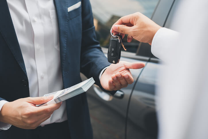 A client buying a new Electric Vehicle, handing over cash to an auto salesperson after automotive sales training.