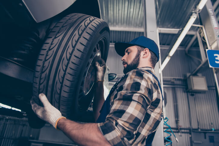After auto mechanic training, An auto repair technician installs a tire on a vehicle.