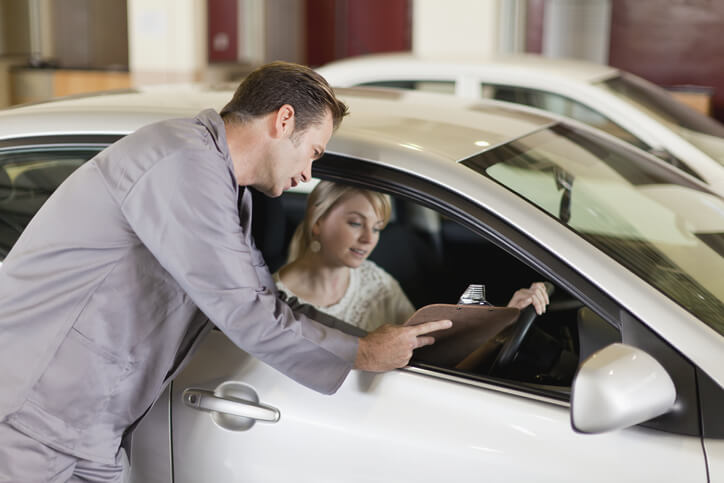 A service advisor discussing the contents of a document with a female customer in a car after automotive training.