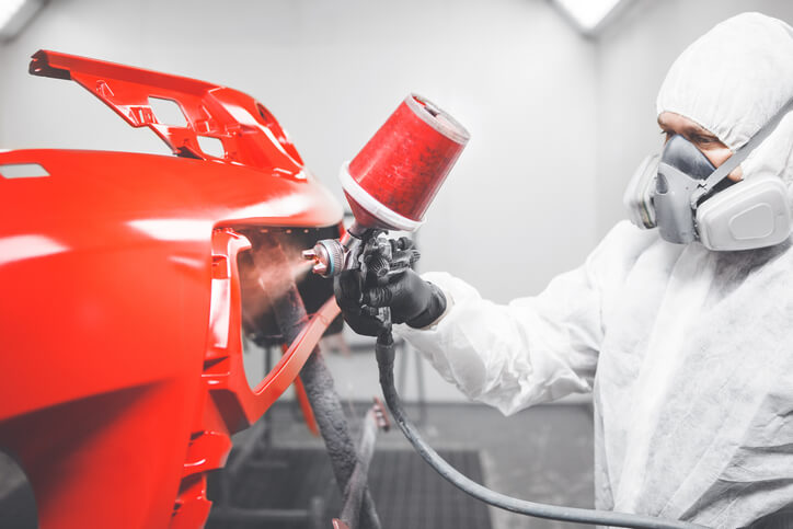 An automotive refinishing prep technician painting a red car with a spray gun