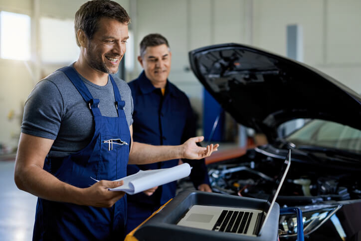 An auto mechanic working the repair shop and talking about auto mechanic jobs with his colleague.