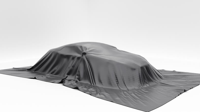 A new car under a silk sheet to be revealed to automotive technology training students.
