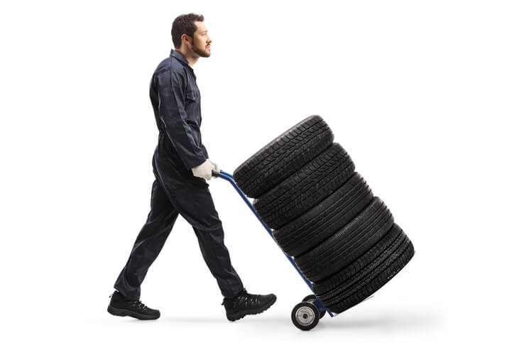 A male auto part technician moves tires with a trolley.