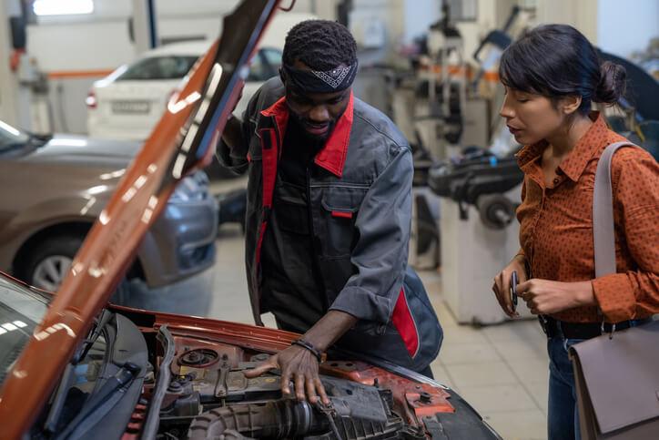 A service advisor training grad collaborating with a repair tech in a garage.