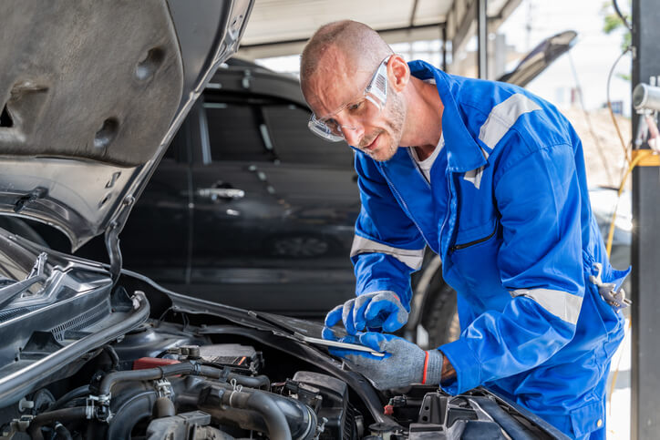 A male auto mechanic examining a car’s engine after auto repair training