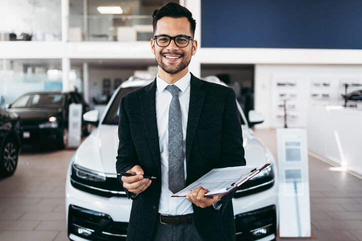 A smiling male car sales manager in a dealership after completing his auto sales training