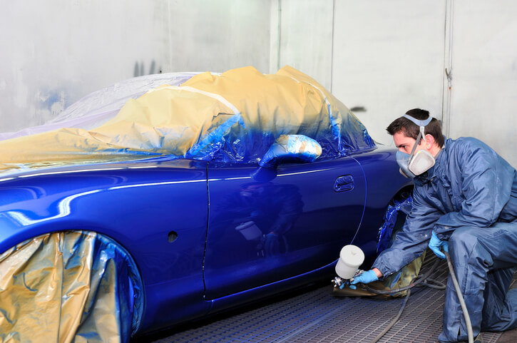 An auto detailing professional spray painting a car after auto detailing training