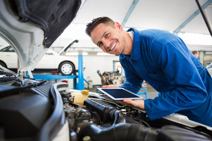 A smiling auto mechanic in a repair shop after completing auto mechanic certification