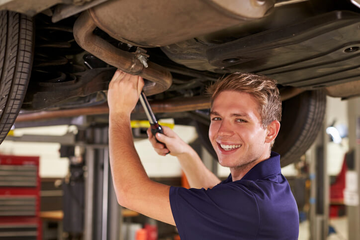 A smiling male auto mechanic working on a vehicle after auto mechanic school