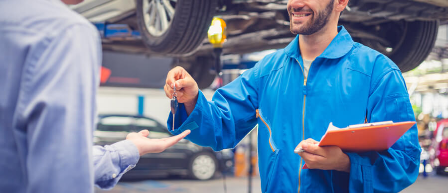 A smiling auto service advisor handing car keys back to a customer after completing his service advisor training