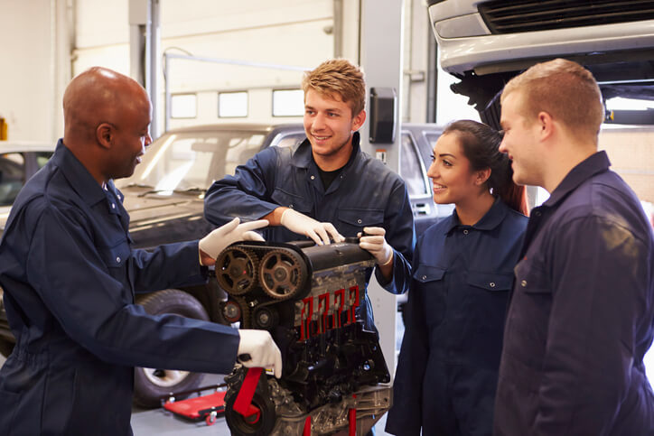 A smiling teacher explaining how engines work to his auto mechanic apprentices