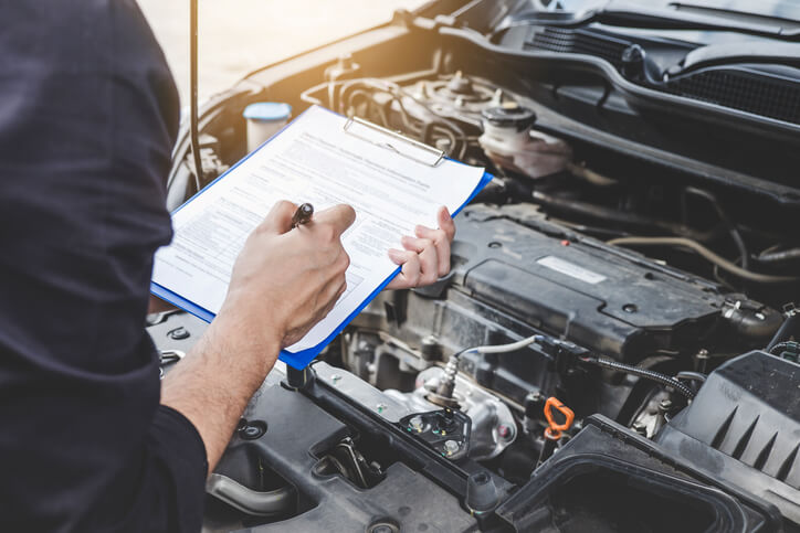 A male diagnostician holding a notepad and examining a vehicle’s engine after graduating from auto mechanic school