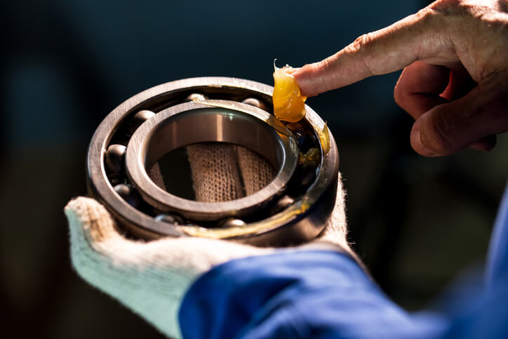 A close-up of an auto mechanic's hand applying a lubricant to a bearing.