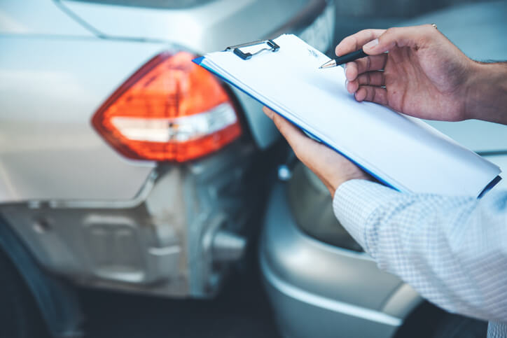 An auto body estimator holding a clipboard assessing the overall condition of a vehicle after completing his auto body estimating training