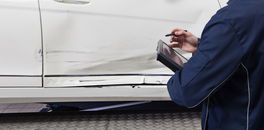 An auto body estimator checking the body of a vehicle after completing his auto body estimating training