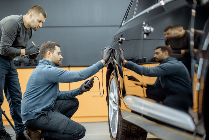 Auto mechanics examining a vehicle’s body for dents and scratches after completing auto mechanic school