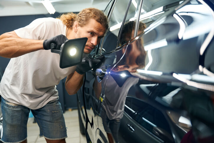 An auto detailing training grad inspecting a car paint job  