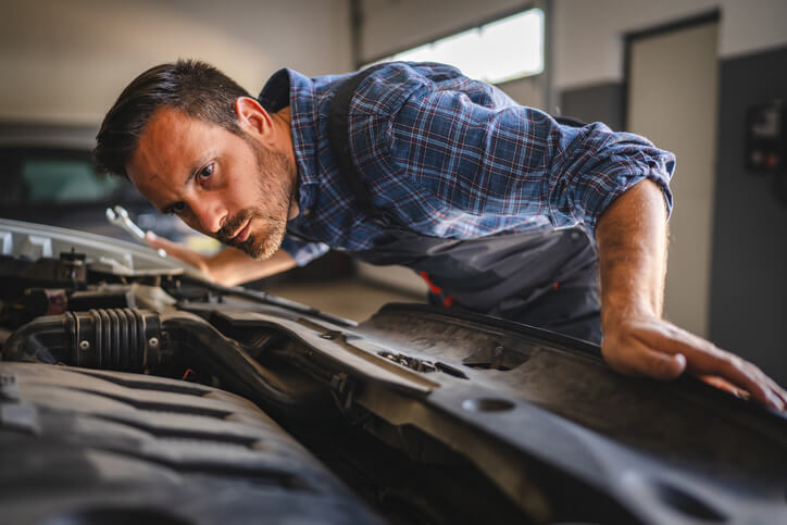 A male auto mechanic examining the engine of a modern vehicle after completing his auto mechanic training