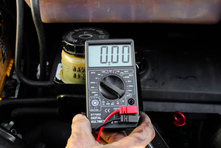 An auto mechanic student using a multimeter to test for parasitic drain
