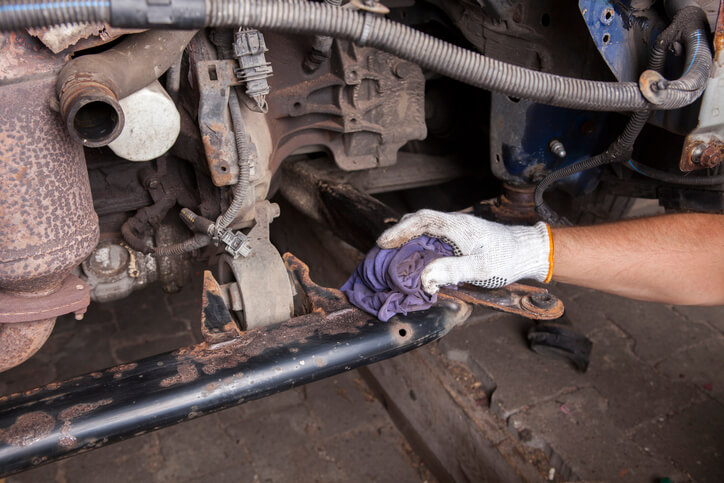 An auto mechanic student removing rusted components in a training shop
