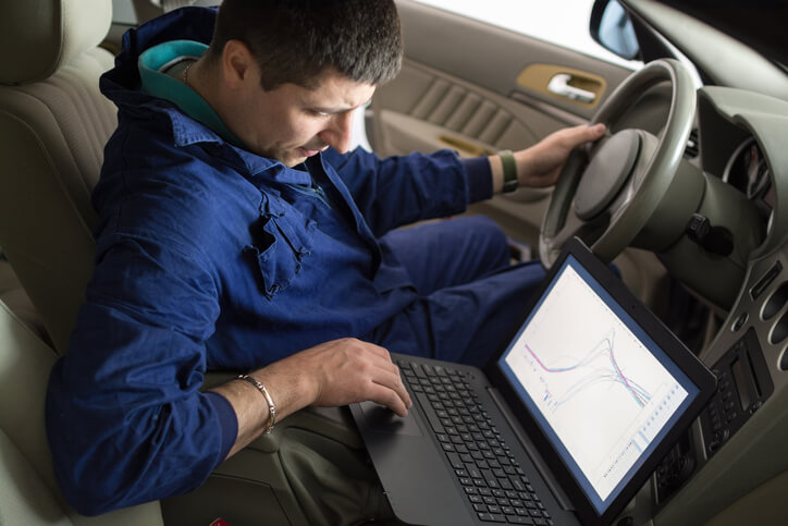 An auto mechanic training graduate diagnosing a vehicle through the vehicle data recorder device connected to the engine