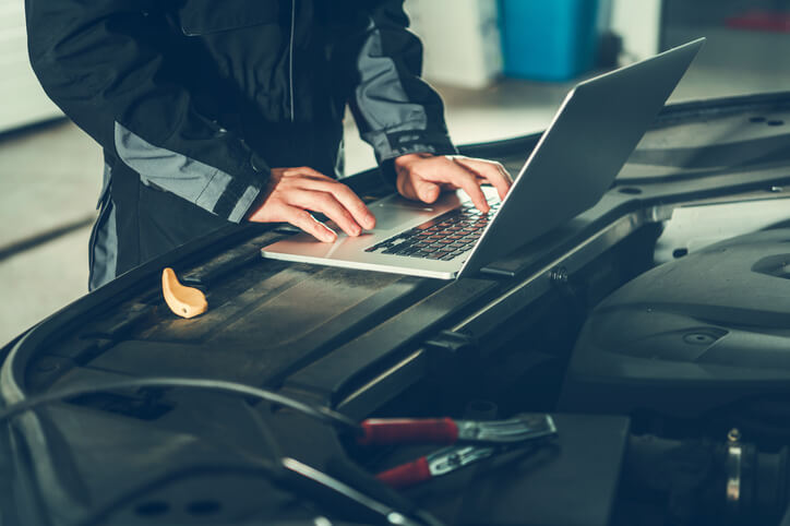 A modern auto mechanic training graduate using a diagnostic scan tool on a car dashboard