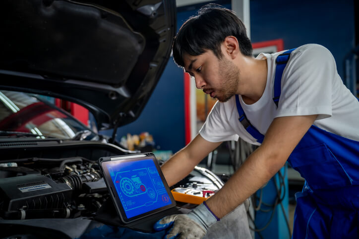 An auto mechanic using a diagnostic tool on an electric car