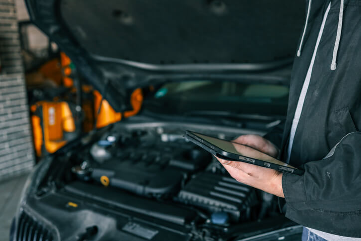 An auto mechanic using a diagnostic tool and reviewing results on a tablet