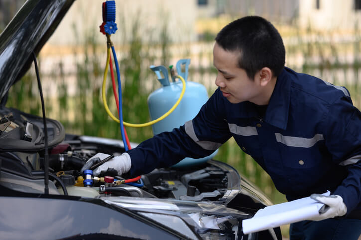 An auto mechanic refilling a car's A/C refrigerant