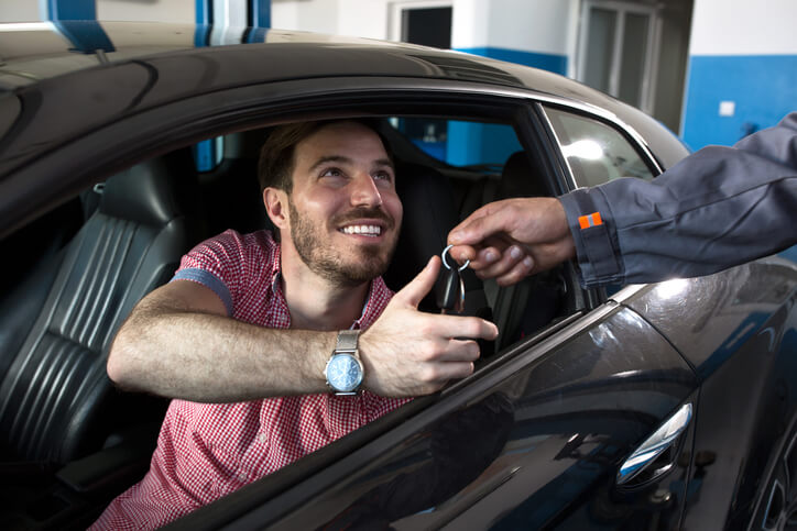 An auto mechanic training student helping a customer at an auto repair shop