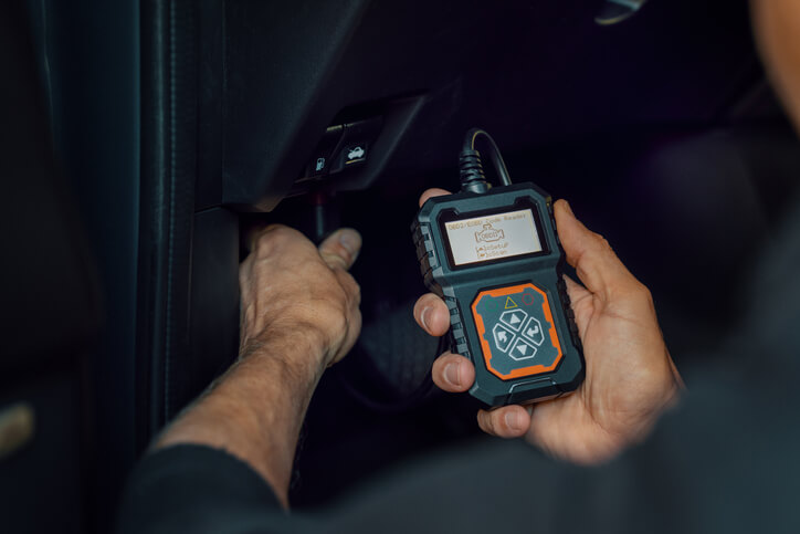 An automotive student using OBD vehicle diagnostics scanner in a repair workshop