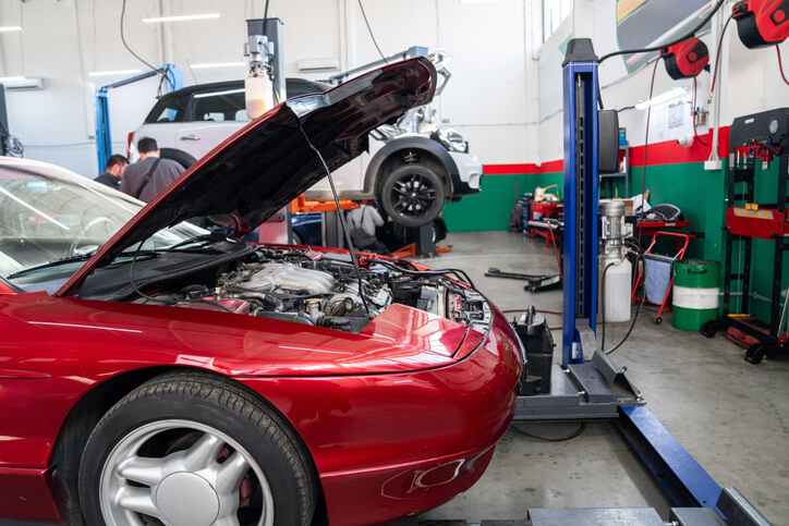 A red sports car undergoing inspection during automotive mechanic training at a professional garage.