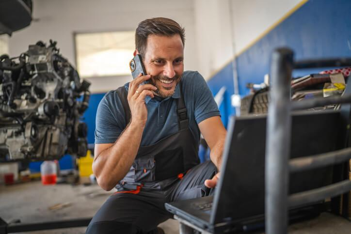 A customer service in auto repair: automotive service technician using laptop and phone in shop