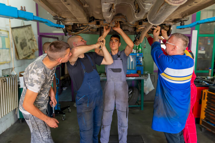 An instructor guiding several students during hands-on auto mechanic training at a college workshop.