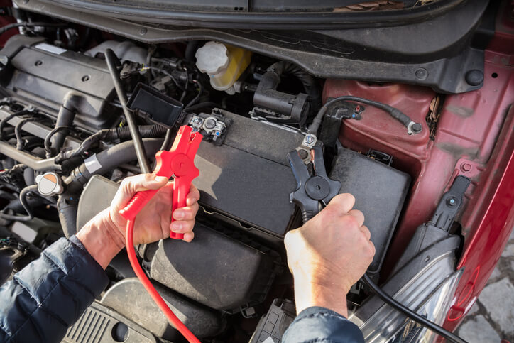 A close-up of hands testing a car battery with jumper cables during auto mechanic training.