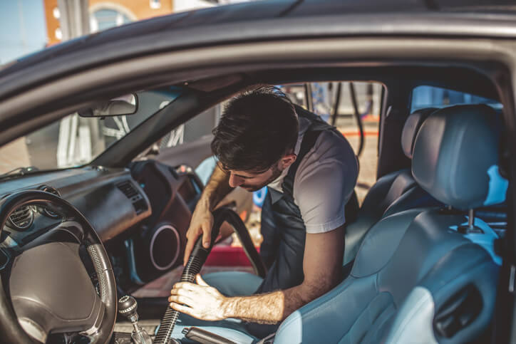 An auto detailing trainee vacuuming a car’s interior