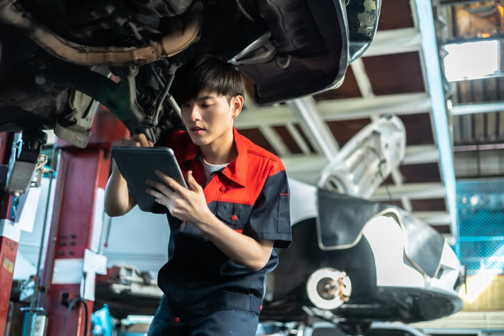 A student in hybrid and electrical mechanic training using a tablet while inspecting a vehicle.