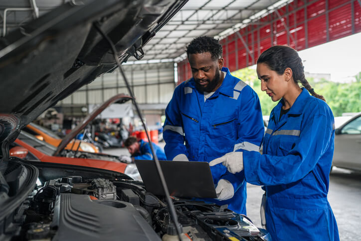 An auto mechanic school in Surrey instructors guiding a student through laptop-based battery testing in the shop.